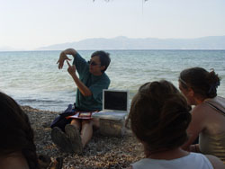 An instructor pointing as part of a class on the beach with the ocean behind him